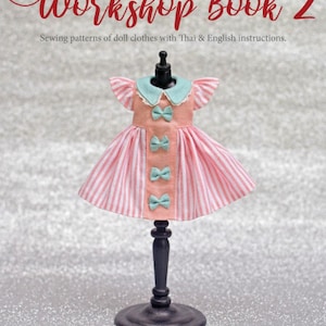 May include: A doll dress on a black mannequin stand. The dress features a peach bodice with a light blue collar and four small light blue bows down the center. The skirt is made of pink and white vertical striped fabric with ruffled sleeves.