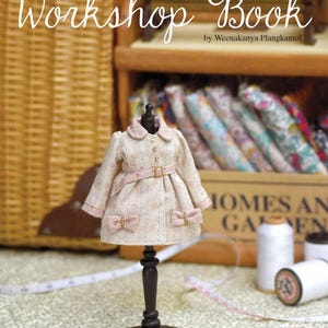 May include: A miniature beige tweed coat with a pink collar, belt, and bow details displayed on a black mannequin stand. The coat features long sleeves and a button-front closure. The text Little Amelie Workshop Book by Weenakanya Plangkamol is visible.