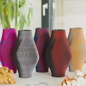 Könnte beinhalten: Eine Sammlung von fünf dekorativen Vasen mit einem einzigartigen, gerippten Design. Die Vasen sind in den Farbtönen Rosa, Grau, Rot und Gelb gehalten. Sie sind auf einer weißen Oberfläche angeordnet.
