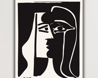May include: Black and white Picasso print of a woman's face. The artwork features a minimalist design with bold lines and shapes. The print is displayed on a wall in a room with a neutral color palette. A vase of dried flowers sits on a wooden surface.