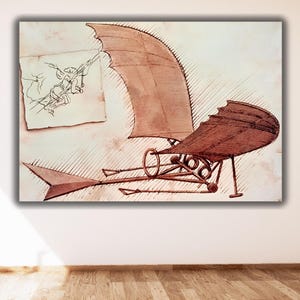 May include: A framed print of a Da Vinci sketch of a flying machine. The artwork features sepia tones, with a detailed drawing of the machine and a smaller sketch of a figure. The print is displayed on a white wall.