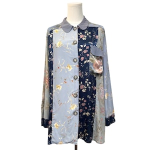 May include: A long-sleeve button-down shirt featuring a patchwork design of light blue and dark navy fabric panels. The shirt displays a floral pattern with yellow and pink blossoms, a solid grey collar, and a single chest pocket on the right side.