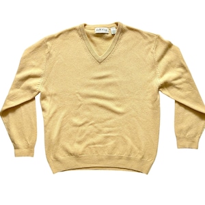 May include: A light tan V-neck sweater with long sleeves. The sweater has a ribbed hem and cuffs. The brand name "ORVIS" is visible on a tag near the neckline. The sweater is made of a soft, knitted material.