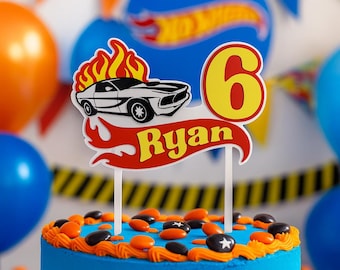 Puede incluir: Una tarta de cumpleaños azul con glaseado naranja y caramelos. Un adorno para tarta presenta un coche de carreras, el número 6 y el nombre "Ryan". Globos naranjas y azules en el fondo.