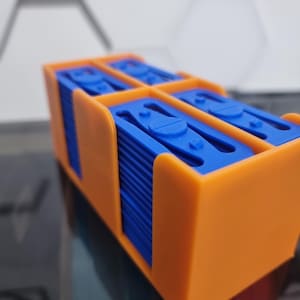 May include: An orange plastic storage case with multiple blue plastic blades stacked inside. The case has a compartment for each blade.