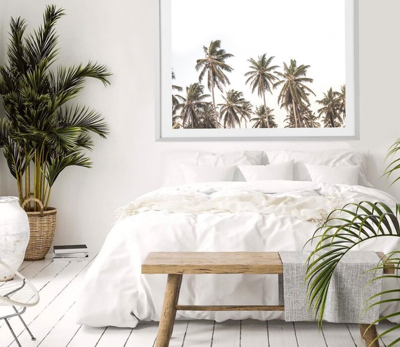 May include: A white bed with white bedding and a wooden bench in front of it. A framed print of palm trees is hanging on the wall behind the bed.