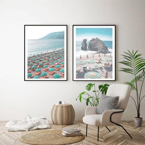 May include: Two framed photographs of a beach scene. The first photo shows a beach with green and white striped umbrellas and lounge chairs. The second photo shows a beach with a rocky cliff and turquoise water.