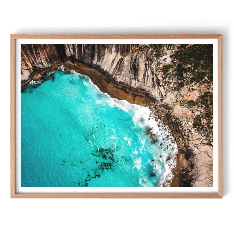 May include: An aerial view of a rocky coastline with turquoise water crashing against the shore. The water is a vibrant blue, and the rocks are a mix of brown and gray.