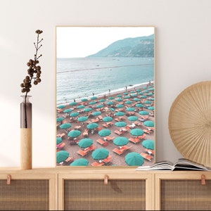 May include: A beach scene with turquoise umbrellas and orange lounge chairs on a sandy beach. The ocean is in the background with a mountain range in the distance.