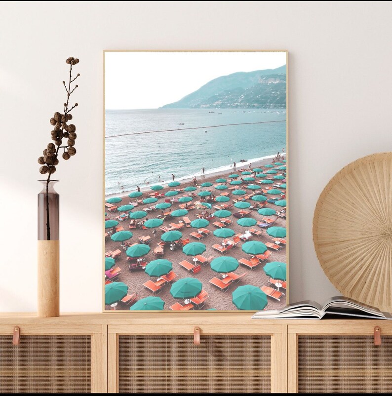 May include: A beach scene with turquoise umbrellas and orange lounge chairs on a sandy beach. The ocean is in the background with a mountain range in the distance.