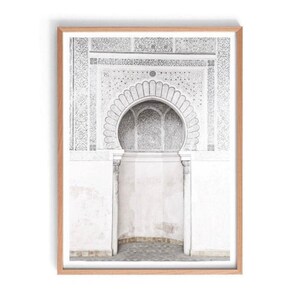 Puede incluir: Un arco blanco con detalles intrincados y una parte superior festoneada, situado contra una pared blanca con una superficie texturizada. El arco est&aacute; enmarcado por un marco de madera.