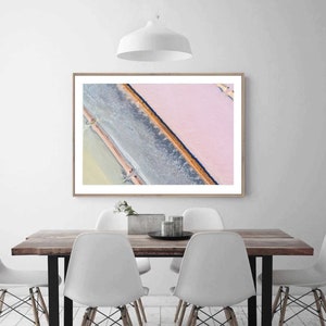 Op de afbeelding: Een luchtfoto van een zoutvlakte met een roze en witte kleurstelling. De zoutvlakte is verdeeld in secties door dunne lijnen water en een donkerdere, bijna zwarte lijn.