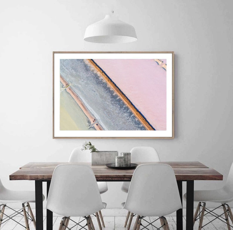 Op de afbeelding: Een luchtfoto van een zoutvlakte met een roze en witte kleurstelling. De zoutvlakte is verdeeld in secties door dunne lijnen water en een donkerdere, bijna zwarte lijn.