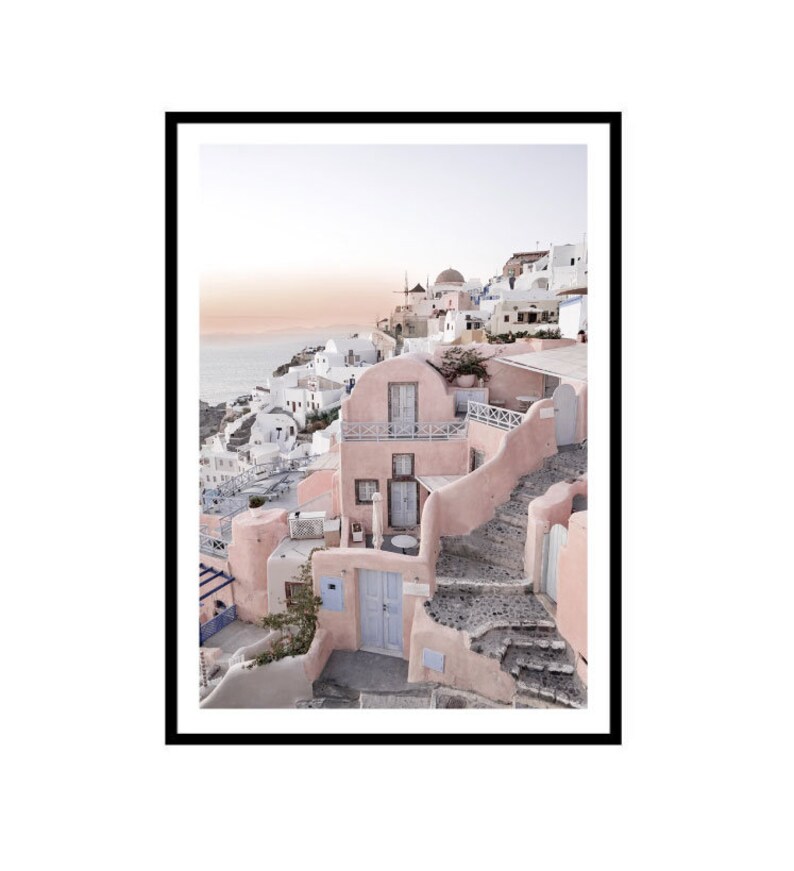 May include: A pink and white building with a blue door and a stone staircase in a village overlooking the ocean. The building has a balcony and a white railing. The sky is a light blue with a few clouds.