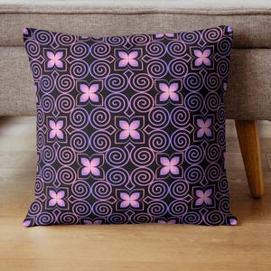 May include: Square cushion featuring a black backdrop with a repeating design of pink and purple floral shapes and swirling lines. The cushion is on a wooden floor next to a grey upholstered chair.
