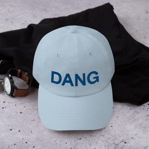Peut inclure: Une casquette de baseball bleu clair avec le mot "DANG" brodé en bleu sur le devant.