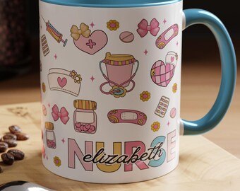 May include: White ceramic mug with a blue interior and handle, decorated with pink and yellow medical-themed illustrations. The word "NURSE" and the name "Elizabeth" are printed on the front. A spoon and a macaron are in the foreground.