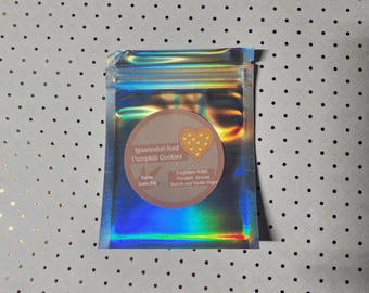 May include: A small, iridescent, resealable bag with a circular label. The label reads "Iguannodon Iced Pumpkin Cookies" with a heart-shaped cookie graphic. The bag is on a white surface with black polka dots.
