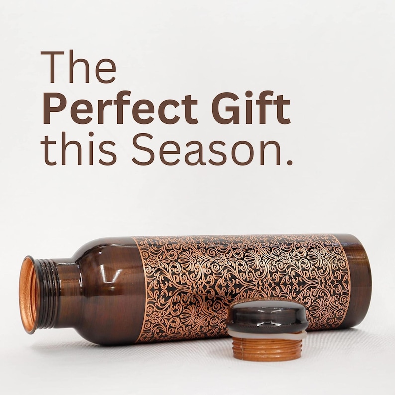 May include: A copper water bottle with a black and gold patterned design. The bottle is lying on its side with the cap off. The text "The Perfect Gift this Season." is visible in the background.