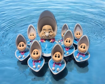 May include: A group of blue and white clam shell figurines with smiling faces. The figurines are floating in a blue pool of water. The largest figurine is a grandmother clam with glasses and a pink dress.