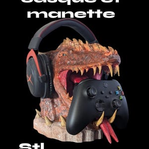 Op de afbeelding: Een 3D-geprinte drakenkopstandaard voor een gaming-headset en een controller. De draak is bruin en oranje met een rode tong. De headset is zwart met rode accenten. De controller is zwart met groene, blauwe en gele knoppen. De standaard is gelabeld met "Support casque et manette" en "STL file".