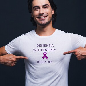 May include: White t-shirt with the text "Dementia with Energy" and a purple ribbon. The text "Keep Up!" is below the ribbon.