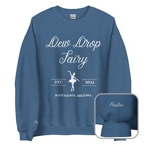 May include: A blue sweatshirt with white text that reads "Dew Drop Fairy" with a ballerina silhouette and the text "DEC 2024 SCOTTSDALE, ARIZONA". The sweatshirt has a white "Pauline" embroidered on the cuff.