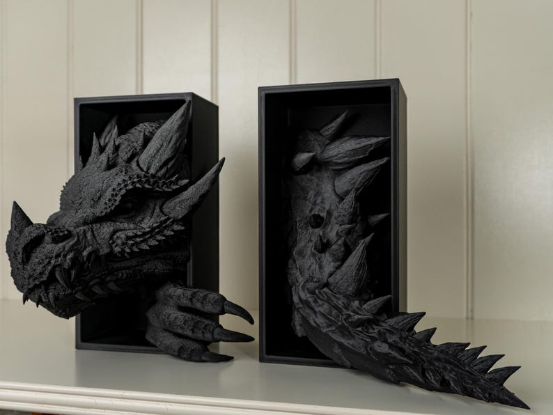 May include: Two black framed wall sculptures of a dragon's head and tail. The dragon's head is facing left and the tail is facing right. The sculptures are made of a textured material that looks like scales.