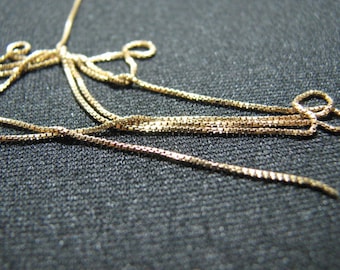 May include: A close-up of a gold chain necklace with multiple strands. The chain is made of small, square links.