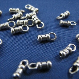 May include: A close-up of a group of silver metal end caps for jewelry making. The end caps have a round shape with a small loop at the top. The end caps are scattered on a blue surface.