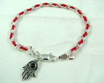 May include: Red string bracelet with a silver Hamsa hand charm with a dark red stone in the center.