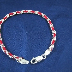 May include: A red and silver bracelet with a braided design. The bracelet has a silver clasp.