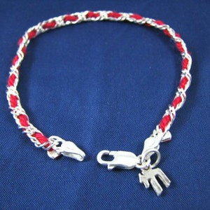 May include: A red and silver braided bracelet with a silver charm. The charm is shaped like a letter M.