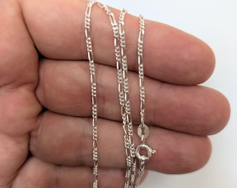 May include: A silver chain necklace with a lobster clasp. The chain is a figaro style with alternating links.