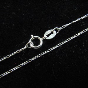 May include: A silver chain necklace with a lobster clasp closure. The chain is a delicate, fine, and flat design.