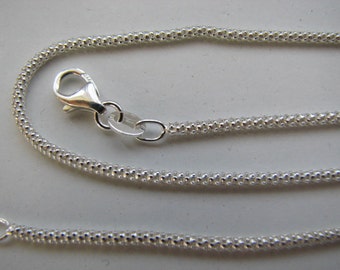 Könnte beinhalten: Eine silberne Kettenkette mit einem Karabinerverschluss. Die Kette besteht aus kleinen, runden Perlen.