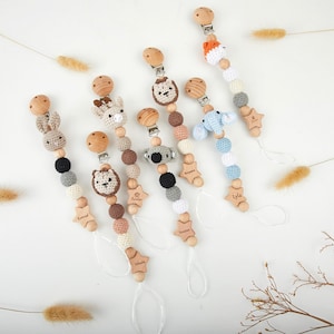Puede incluir: Seis clips para chupetes hechos a mano con cabezas de animales de ganchillo, cuentas de madera y dijes de madera en forma de estrella. Cada clip incluye un cierre de metal y un lazo de cordón blanco. Los animales incluyen conejo, león, jirafa, koala, elefante y zorro.