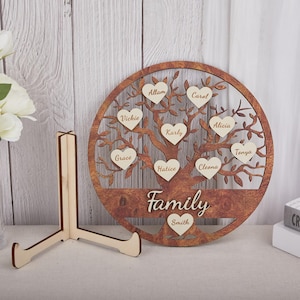 Könnte beinhalten: Ein hölzerner Familienstammbaum mit kreisförmigem Design. Der Baum hat herzförmige Blätter mit Namen und das Wort "Family" an der Basis. Inklusive eines Holzständers zur Präsentation.