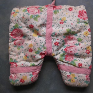Puede incluir: Un par de guantes para horno de color rosa y blanco con estampado floral y diseño acolchado. Los guantes tienen un ribete rosa y están hechos de una tela de algodón suave.