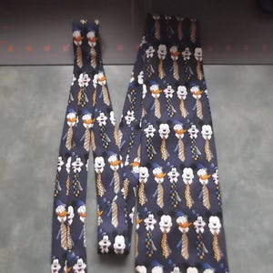 May include: A dark navy blue necktie featuring a repeating pattern of Mickey Mouse and Donald Duck characters. Each character is depicted wearing a different patterned necktie, including stripes, polka dots, and checkered designs in yellow and blue.