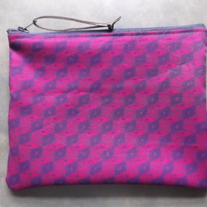 May include: A pink and purple zippered pouch with a geometric pattern. The pouch has a black strap.