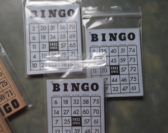 Può includere: Tre cartelle del bingo con numeri neri su sfondo bianco. Le cartelle sono in sacchetti di plastica. Le cartelle hanno la parola "BINGO" in alto e la frase "SPAZIO LIBERO" al centro.