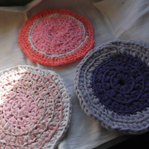 Può includere: Tre sottobicchieri circolari fatti a mano, nei toni del rosa, corallo e viola. Ogni sottobicchiere presenta un design a spirale, con i colori che vanno dal centro ai bordi. I sottobicchieri sono realizzati in un materiale morbido e strutturato.