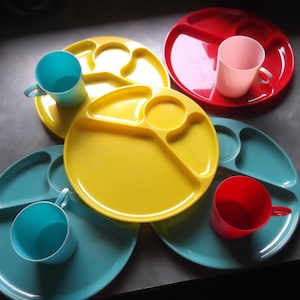 May include: Four divided plates in red, yellow, blue and teal with four matching cups in pink, blue, red and blue. The plates and cups are made of plastic.