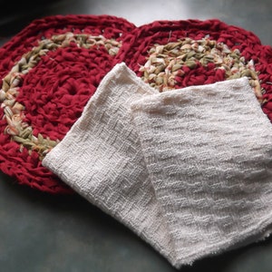 May include: Two red and green crocheted rugs with a white crocheted dishcloth on top.