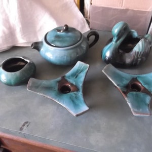 Può includere: Un set di cinque pezzi in ceramica vintage in tonalità di blu e verde. Il set comprende una teiera, un creamer, un piatto a forma di cigno e due portacandele triangolari.