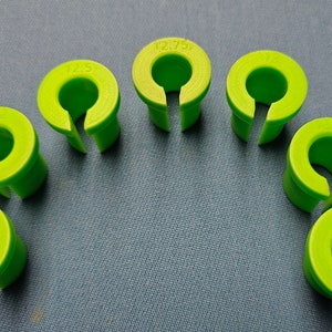 以下が含まれることがあります： サイズが異なる8つのライムグリーンのケーブルクランプ。11/8、12.5、12.75、13.5、14と表示されています。