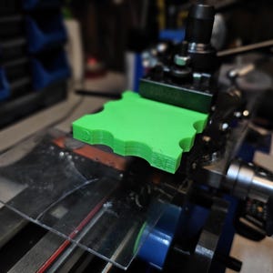 以下が含まれることがあります： テクスチャ加工された表面を持つ緑色のプラスチック製のオブジェクトが、金属製の旋盤に取り付けられています。オブジェクトは旋盤で回転しており、金属の削りくずが見えます。