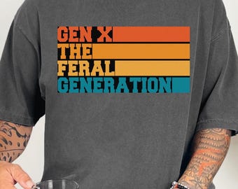 Puede incluir: Una camiseta gris oscuro con un gráfico de estilo vintage que dice "Gen X The Feral Generation" en texto blanco y naranja con un fondo a rayas.
