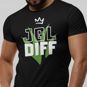 Puede incluir: Camiseta negra con la inscripción blanca "JGL DIFF", coronada con una corona y detalles verdes. La camiseta es de cuello redondo y manga corta.